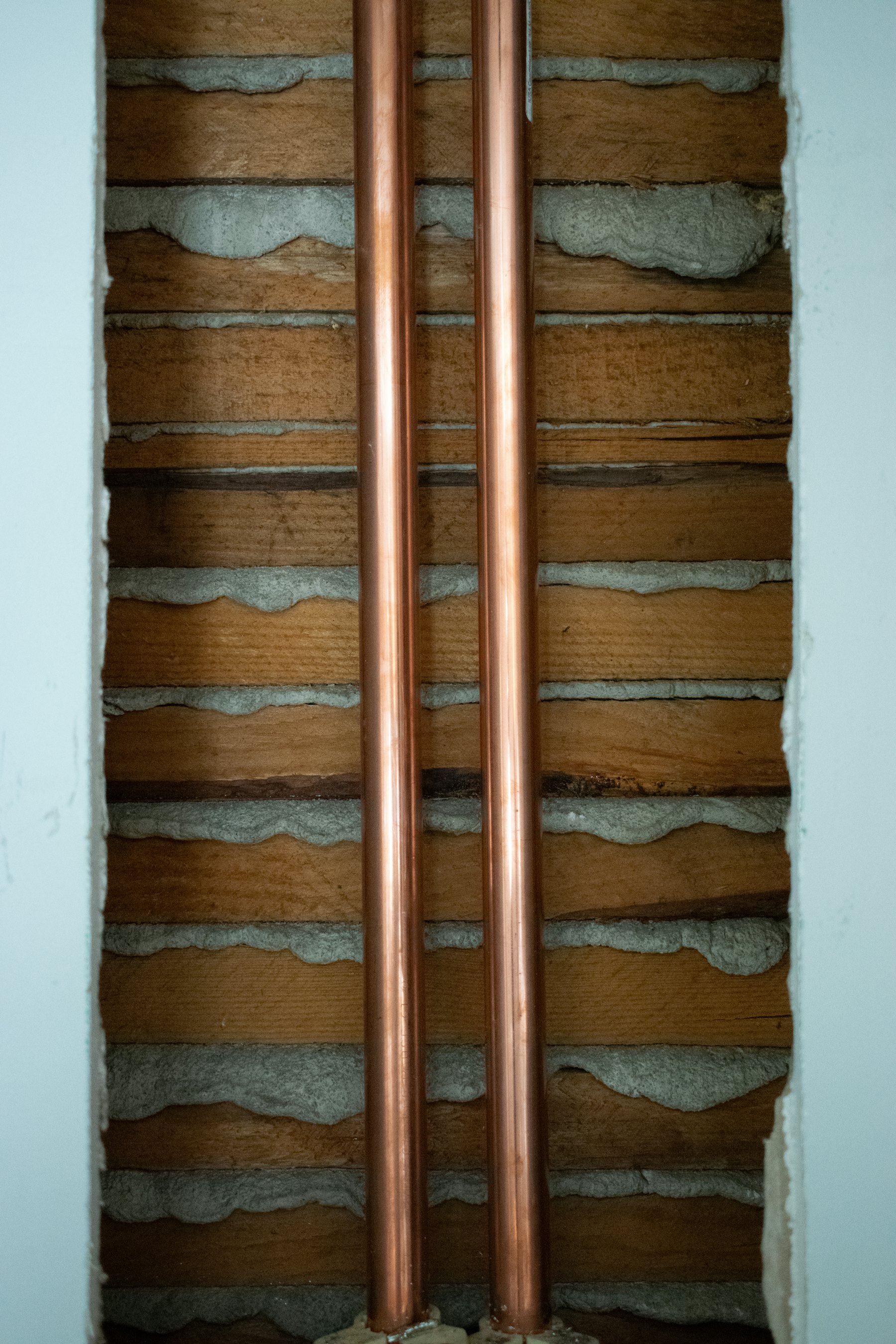 Twin copper pipes running down a wall